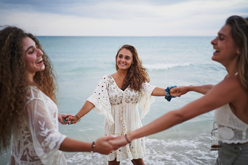 Three women making circle and turning together while laughing and having fun on beach