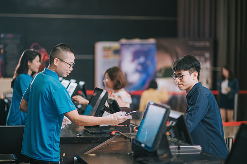 asian chinese young man ordering snack popcorn mineral water at bar counter at movie theater before the cinema movie show time