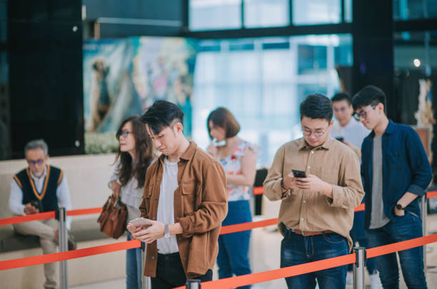 istock group of Asian Chinese young customer looking at smart phone while waiting in line in front ticket counter buying movie tickets and  popcorns drink contactless payment before movie show time at movie theater cinema 1328885861