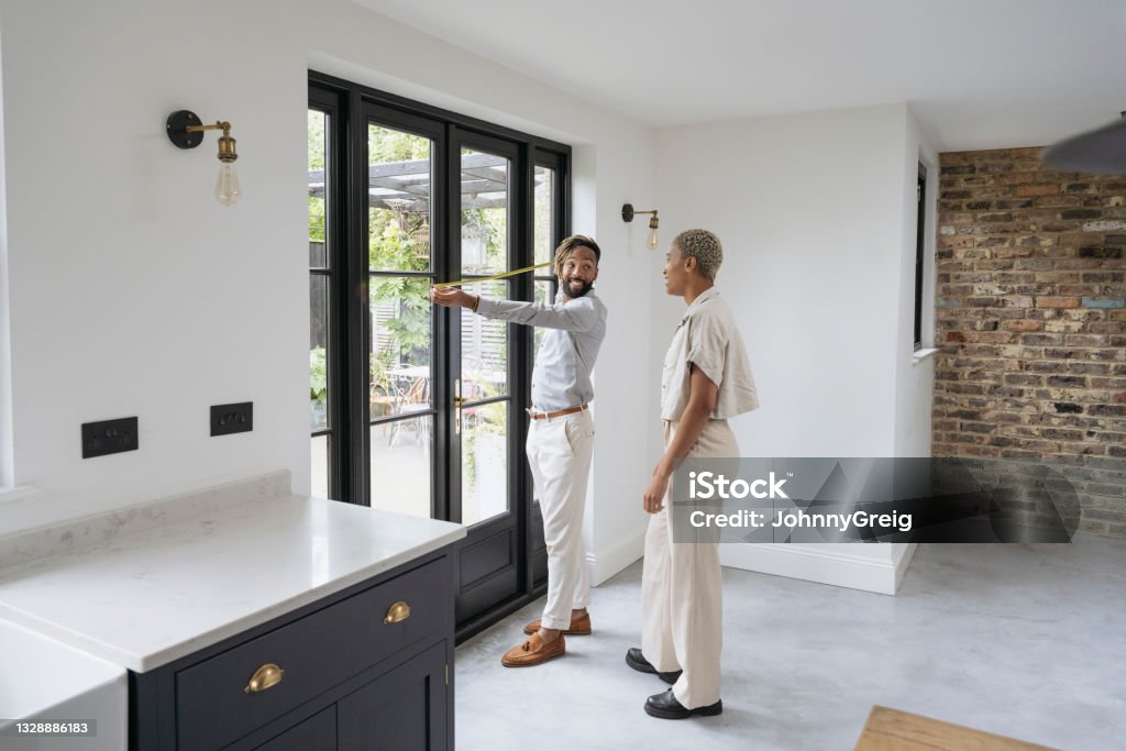 Prospective buyers taking measurements in luxury home Full length side view of smiling mid adult Black couple measuring width of doorway leading outside to patio during real estate showing. Measuring Stock Photo