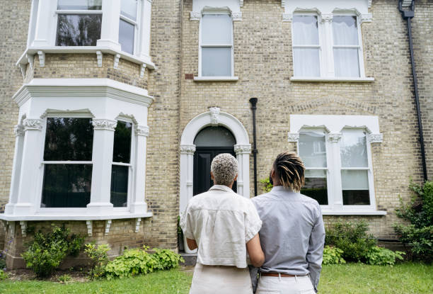 Portrait of new homeowners admiring their investment Rear view of mid adult Black couple standing arm in arm and looking at facade of restored 1890 double fronted Victorian house. victorian houses exterior stock pictures, royalty-free photos & images