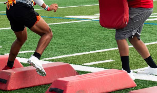 Football player running sideways over barriers about to take a hit from his coach Football player running sideways over red barriers while taking a hit by the coach with a red pad at summer camp sports training camp stock pictures, royalty-free photos & images
