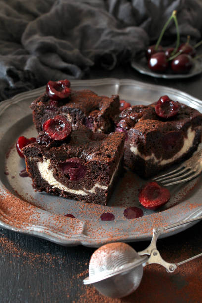 istock Chocolate brownie with cheese cream and cherry on dark background. 1328887390