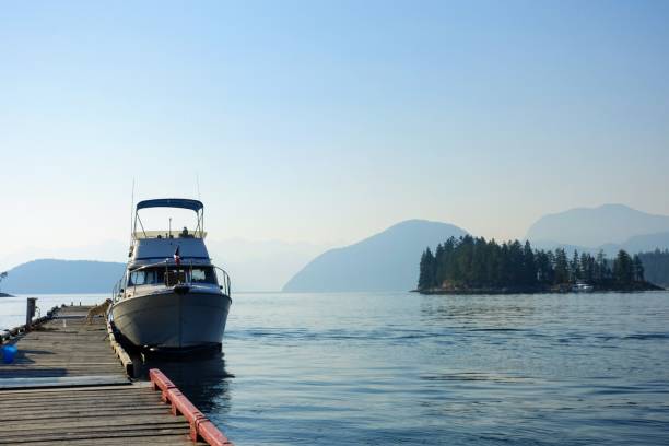 una foto di un motoscafo bayliner solitario legato a un molo, con il bellissimo oceano e le isole coperte di foreste sullo sfondo, a egmont, sulla sunshine coast, british columbia, canada - bayliner foto e immagini stock