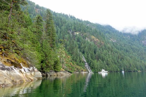 A boat anchored in front of a beautiful waterfall surrounded by rugged forests and mountains in princess Louisa inlet, British Columbia, Canada