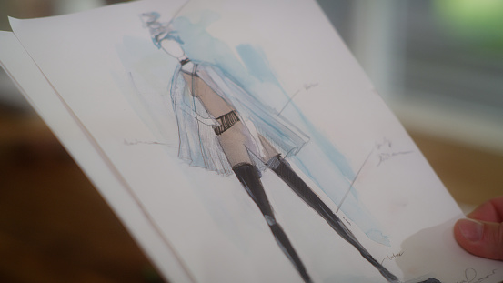 Fashion illustration in process in the artist's studio. Watercolour painting holded by author's hand
