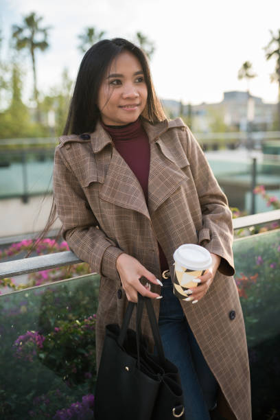 istock Young Asian girl waiting leaning on a railing with a coffee 1328894814