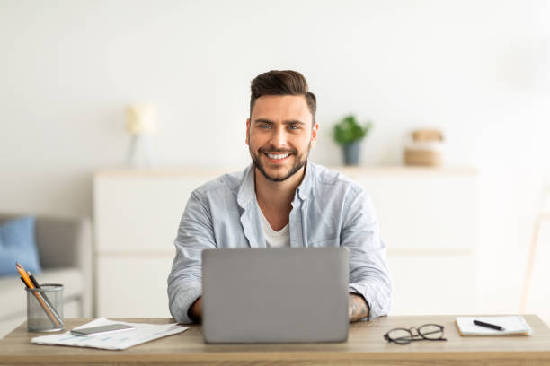 istock Successful freelancer. Happy man sitting at workplace with laptop computer, smiling and looking at camera 1328898497