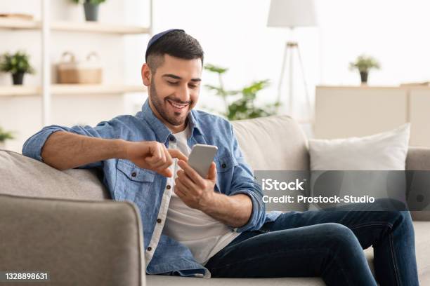 Smiling Jew Man Using Smart Phone Sitting On Couch Stock Photo - Download Image Now - Mobile Phone, People, Men