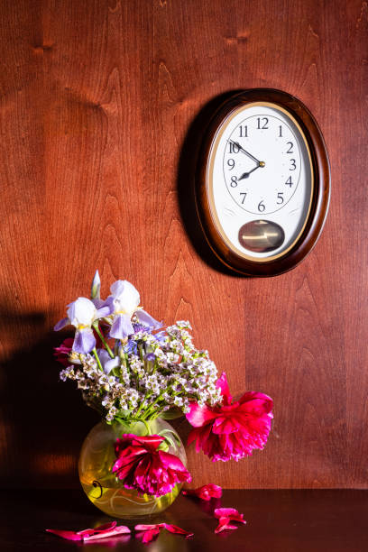 istock wall clock and withered flowers in vase on brown 1328899887
