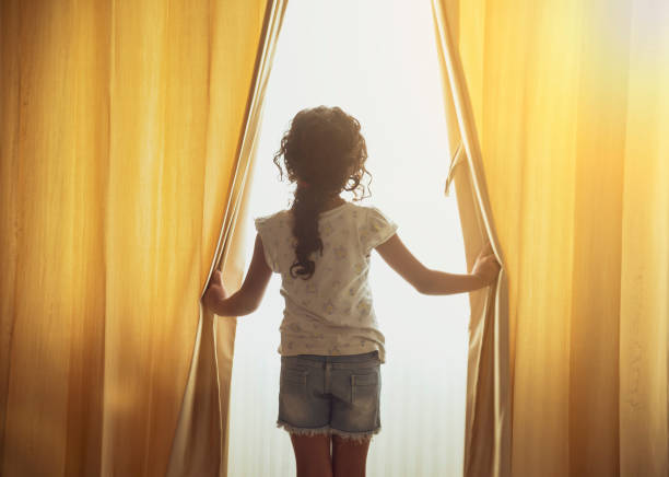 Beautiful Little girl looking through a house window