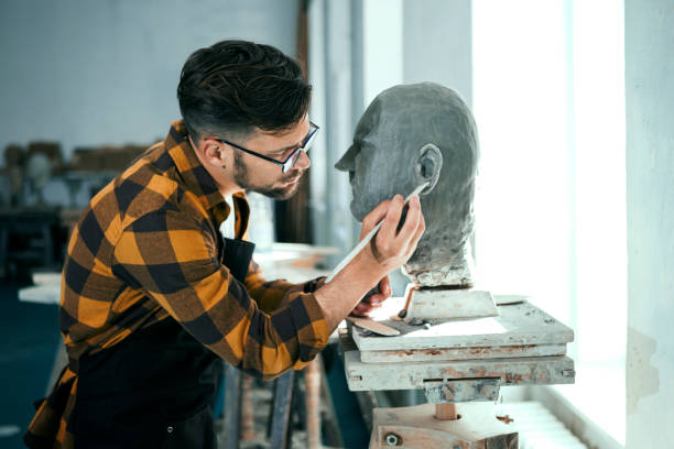 istock Young man sculpting head out of clay in studio with work tool 1328918208