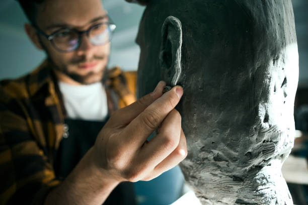 istock Young man sculpting head out of clay in studio working on ear 1328918361