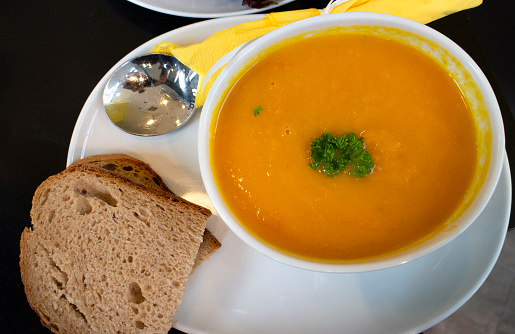 Bowl of fresh carrot and pumpkin soup with a slice of brown bread