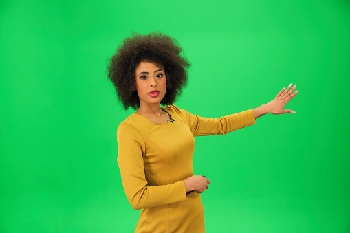 Young weather woman in front of a green background with small remote in her other hand.