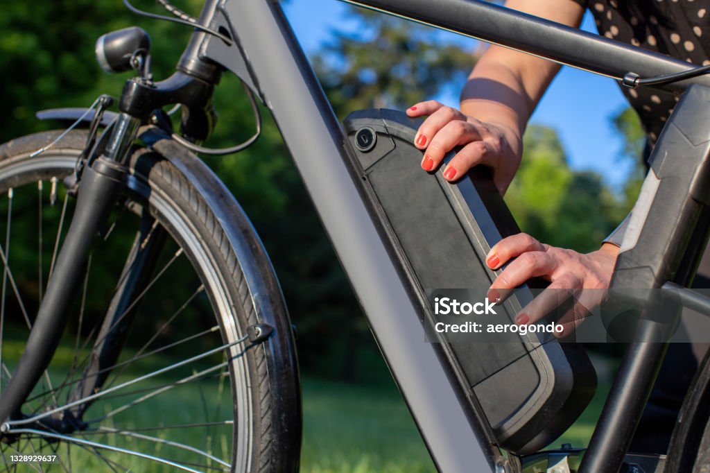 detail of woman holding an electric bike battery mounted on frame woman holding an electric bike battery mounted on frame Electric Bicycle Stock Photo
