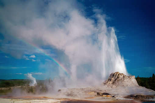 Two thermal geysers erupt and create a rainbow with their mist