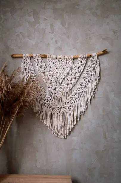 Photo of Handmade macrame 100 cotton wall decoration with wooden stick hanging on a white wall.