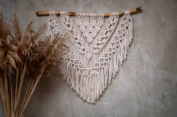 Photo of Handmade macrame 100 cotton wall decoration with wooden stick hanging on a white wall.