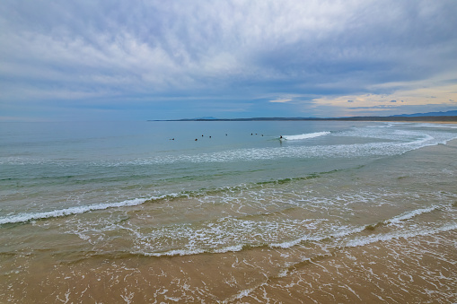 The long sweeping beach with surfers at Broulee on the South Coast of NSW, Australia.