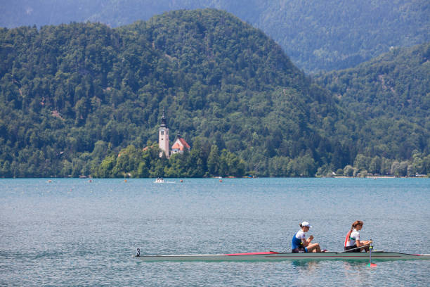 zwei junge erwachsene, ruderinnen, auf einem vierer ohne steuermann, einem ruderboot, das rudertraining für einen aviron-wettbewerb auf dem bleder see im sommer in slowenien. - riemenrudern stock-fotos und bilder