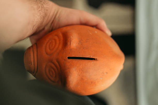 Close up shot of a Young man’s hand holding a clay piggy bank next to his hip