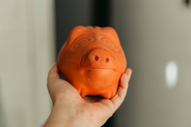 Close up shot of a Young man’s hand holding a clay piggy bank up in the air with its nose being spot on in focus