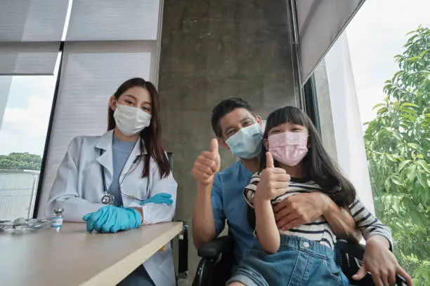 Thumb up selfie Portrait, wheelchair male patient, girl who is his daughter. and female doctor smiling after taking health check and vaccination against coronavirus (COVID-19) at a hospital clinic