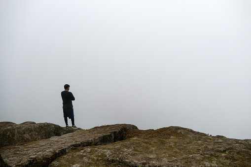 Man standing on cliff in a valley, looking at the mist.