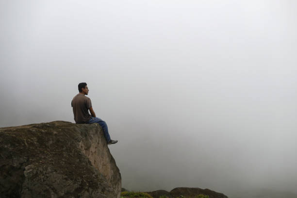 istock Man sitting on a cliff in a valley, looking at the fog. 1328993383
