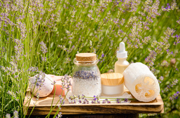 divers produits de spa de beauté sur plateau en bois dans un champ de lavande en fleurs par une journée d’été ensoleillée. sel de bain, barre de savon, crème de jour, hydratant, bombe de bain, huile aromatique. vue latérale. - multi well trays photos et images de collection