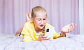 A Caucasian teenage girl with a phone in her hands, lying on the bed, blogging.