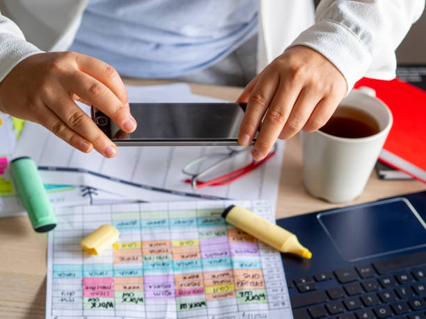 frau scannt mit einem telefon ein planungsdokument auf einem schreibtisch - working at home calendar laptop women stock-fotos und bilder