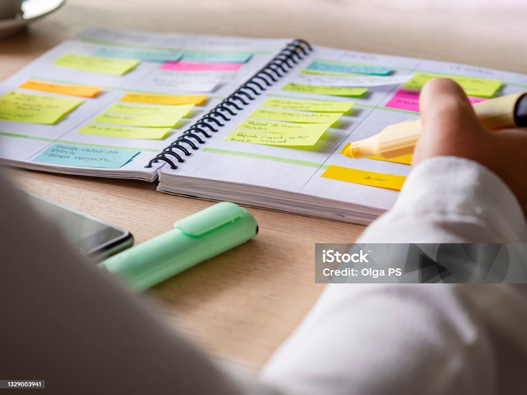 agenda organize with color-coding sticky for time management Close-up of agenda organize with color-coding sticky notes for time management. Productive schedule for appointments and reminders. Hand holding a yellow highlighter marker. Organization and planning Personal Organizer Stock Photo
