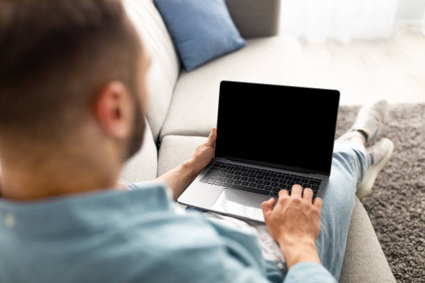 istock Unrecognizable young man using laptop on comfy sofa at home, mockup for website design on screen 1329005341
