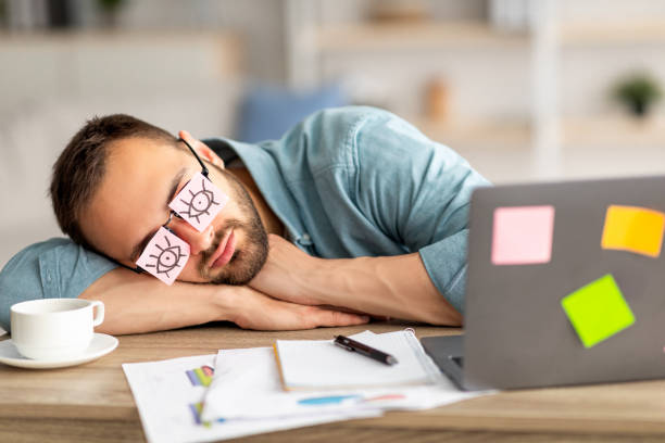 leniwy bezproduktywny młody facet noszący śmieszne karteczki samoprzylepne z otwartymi oczami na okularach, śpiący w miejscu pracy - student sleeping boredom college student zdjęcia i obrazy z banku zdjęć
