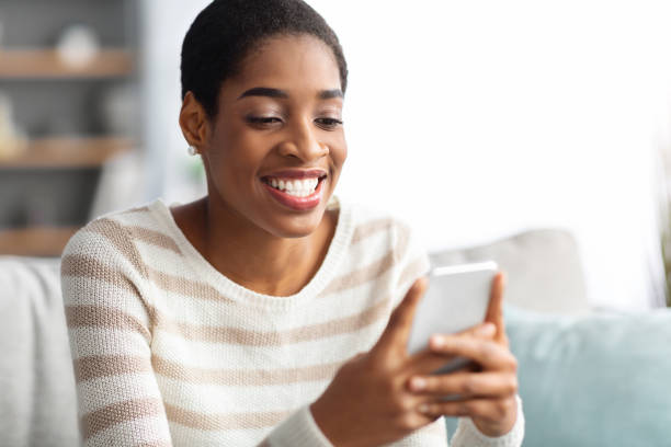 istock Cheerful Black Woman Using Smartphone While Relaxing On Couch At Home 1329006132