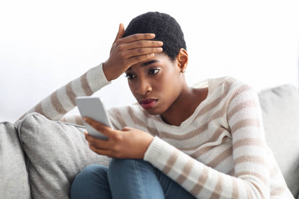 istock Concerned Black Lady Looking At Smartphone Screen At Home And Touching Head 1329006179