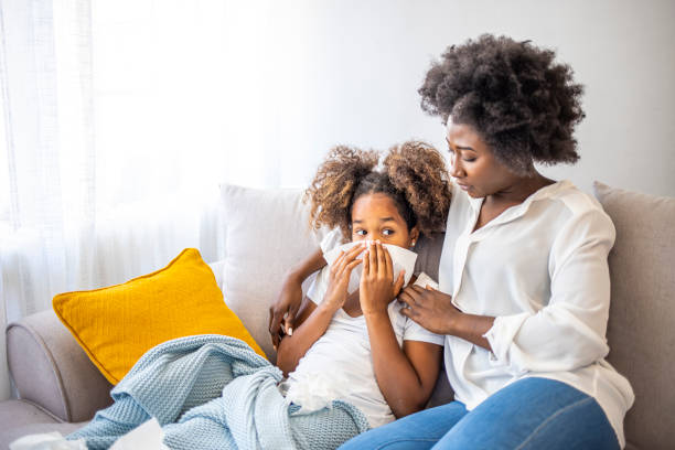 мать проверяет больную дочь, лежащую в постели. - cold and flu flu virus sneezing illness стоковые фото и изображения