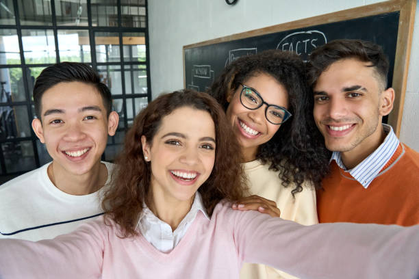 istock Four multiracial cheerful happy students taking selfie in classroom. 1329013223