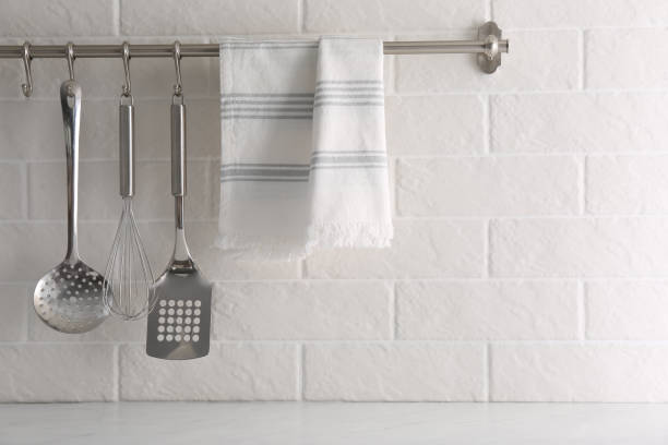 istock Soft kitchen towel and utensils hanging on rack near white brick wall 1329015260
