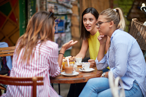 group of young adult caucasian female friends talking, sitting in outdoor cafe, drinking coffee. serious talk, conversation
