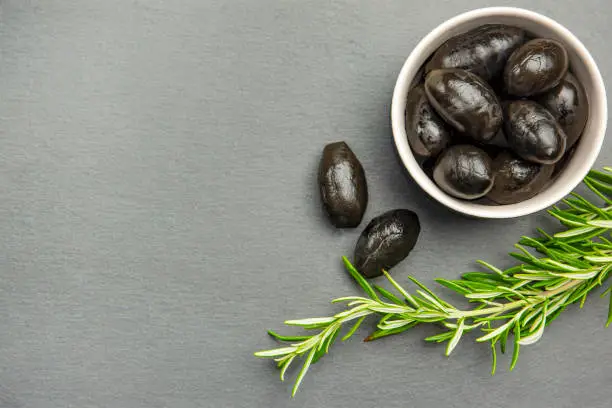 Black olives. Bella di cerignola Italian olives. Colored olives and a sprig of rosemary lie on a black stone countertop. Culinary banner or poster for advertising with place for text.