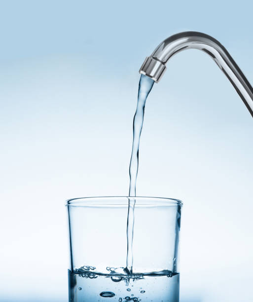 istock Filling glass with water from tap on light blue background 1329019912