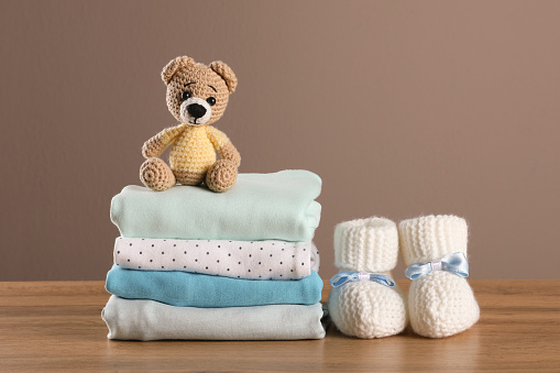Pila de ropa de bebé, botines y juguetes sobre mesa de madera sobre fondo marrón, espacio para texto photo