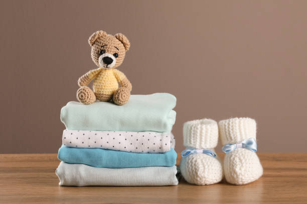 Stack of baby boy's clothes, booties and toy on wooden table against brown background, space for text Stack of baby boy's clothes, booties and toy on wooden table against brown background, space for text baby clothing stock pictures, royalty-free photos & images