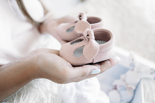 Small pink shoes for unborn baby on belly of pregnant woman.