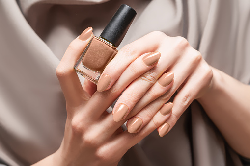 Female hand with beige nail design. Brown nail polish manicure. Woman hand hold beige nail polish bottle