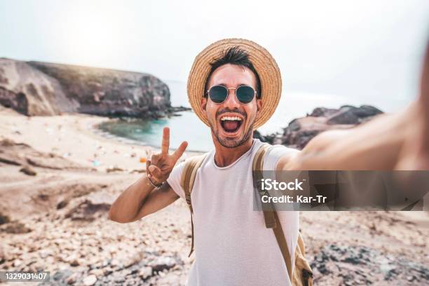 山で自分撮りの肖像画を撮るバックパックを持つ若者 ビーチで夏休みを楽しむ笑顔の幸せな男 カメラに勝利の手のシンボルを示すミレニアル世代 若者と旅 - 旅行のストックフォトや画像を多数ご用意