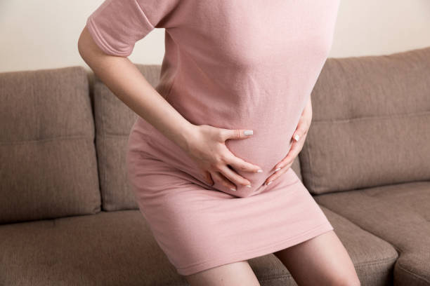 istock Pregnant Lady Having Massaging Lower belly Sitting On Sofa Indoor. Pregnancy Problems Concept. Maternity healthcare 1329033584